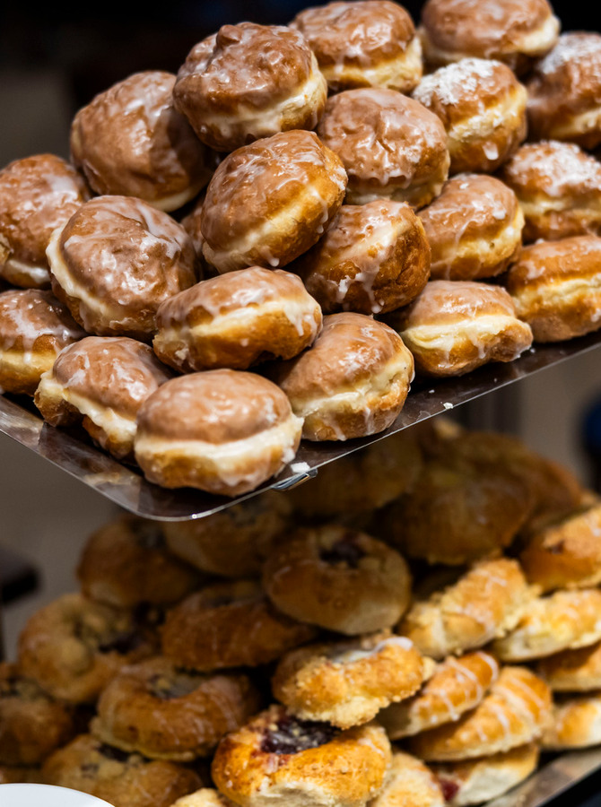 Gestapelte glasierte Krapfen und verschiedene Gebäckstücke auf einer zweistöckigen Metall-Etagère am Frühstücksbuffet des Hotels.
