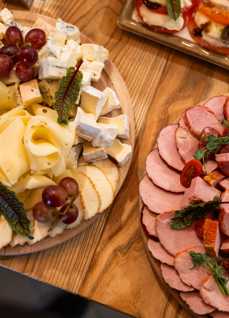 Käse- und Wurstplatten auf Holzbrettchen mit Brie, Blauschimmel- und Schnittkäse, Aufschnitt, Crackern, Trauben und Cherrytomaten