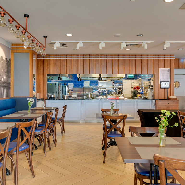 Restauracja hotelowa z otwartą kuchnią, drewnianą ścianą, niebieską kanapą, stołami i świeżymi kwiatami