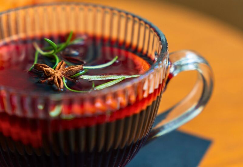 Glass cup of hot spiced beverage garnished with star anise and rosemary on wooden table with dark napkin