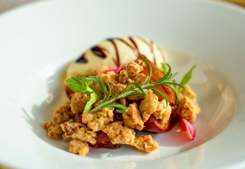 Dessert with crunchy crumble, fresh herbs, and a scoop of vanilla ice cream drizzled with chocolate sauce.
