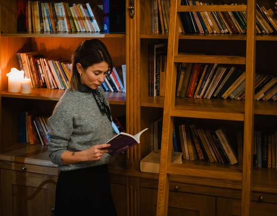 ركن مكتبة فندقي دافئ مع أرفف خشبية وسُلّم، إضاءة بالشموع ونزيل يقرأ كتابًا