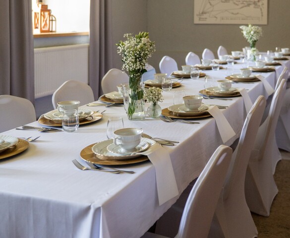 Long elegant banquet table with white linens, gold chargers, teacups and baby’s-breath centerpieces under a wooden chandelier
