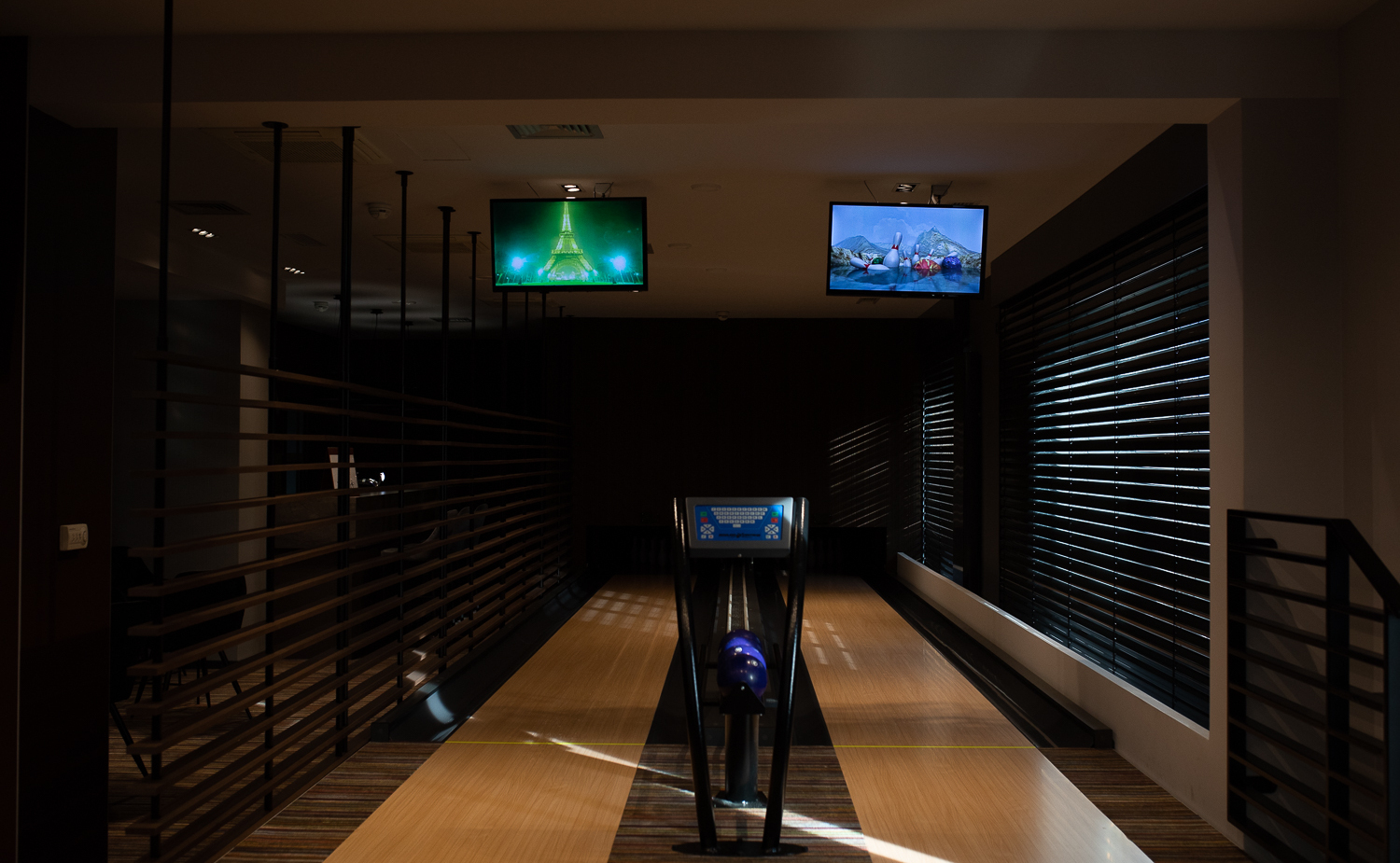 Private Hotel-Bowlingbahn mit polierten Holzbahnen, Kugelrückgabe, lila Kugeln, Decken-TVs und stimmungsvollem Licht
