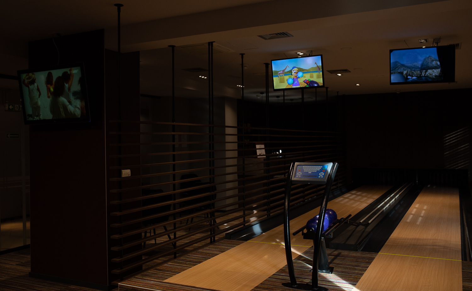 Hotel-Bowlingbahn mit poliertem Holzbelag, violetten Kugeln im Rücklauf, digitaler Anzeige und gedämpfter, gemütlicher Beleuchtung