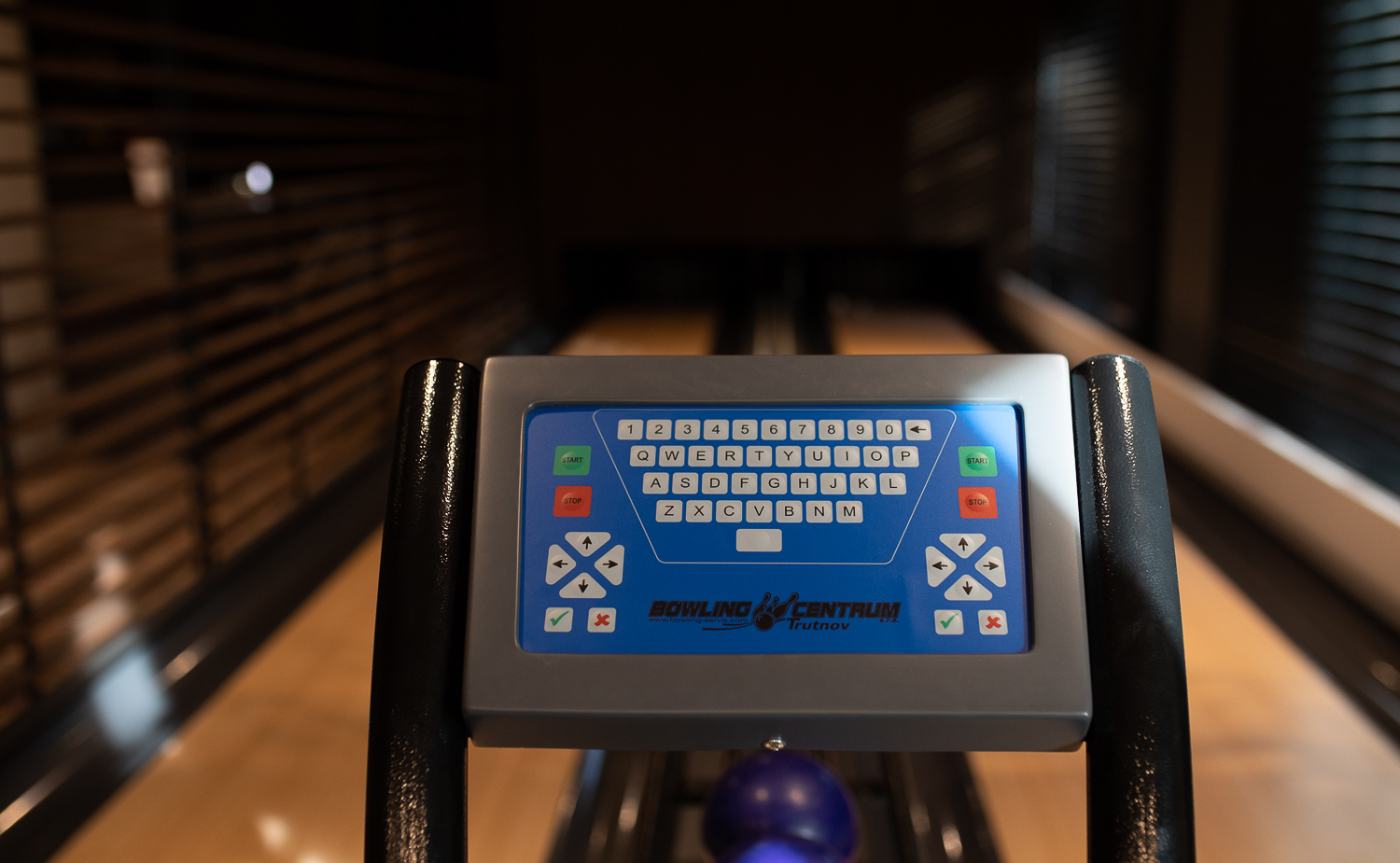 Steuerfeld einer Bowlingbahn mit Tastatur, Start/Stop-Knöpfen und violetten Kugeln auf polierten Bahnen bei warmem, gedämpftem Licht