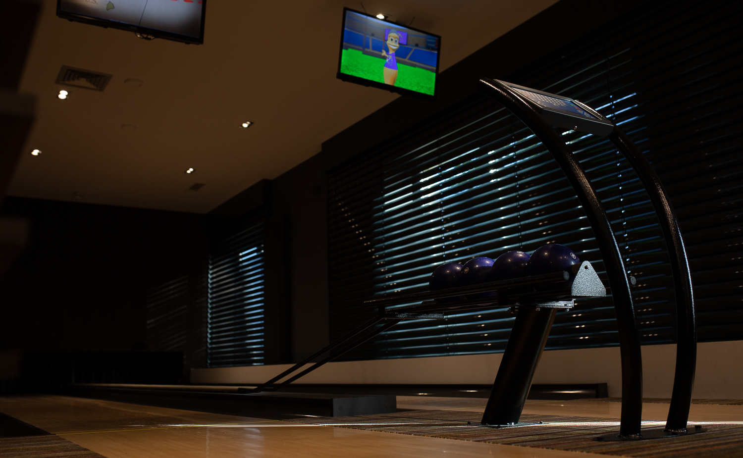 Hoteleigene Bowlingbahn mit polierten Holzbahnen, Ballrückgabe mit blauen Kugeln, Deckenbildschirmen und gedämpfter Stimmung.