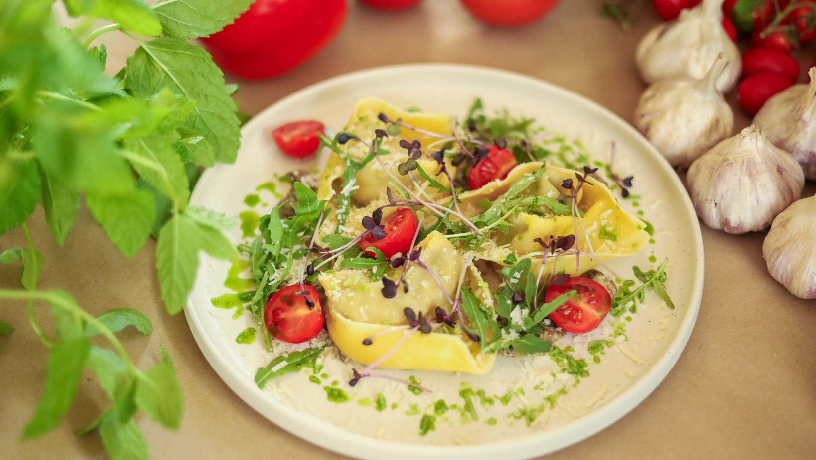Čerstvé plněné ravioli s cherry rajčaty, rukolou, klíčky a nastrouhaným sýrem pokapané bylinkovým olejem na bílém talíři