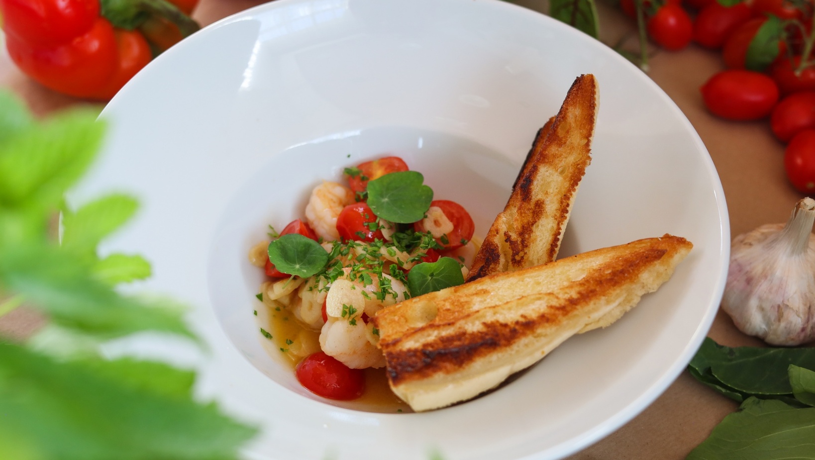 Krevety s cherry rajčaty v aromatickém vývaru, posypané bylinkami a klíčky, se dvěma plátky grilovaného česnekového chleba