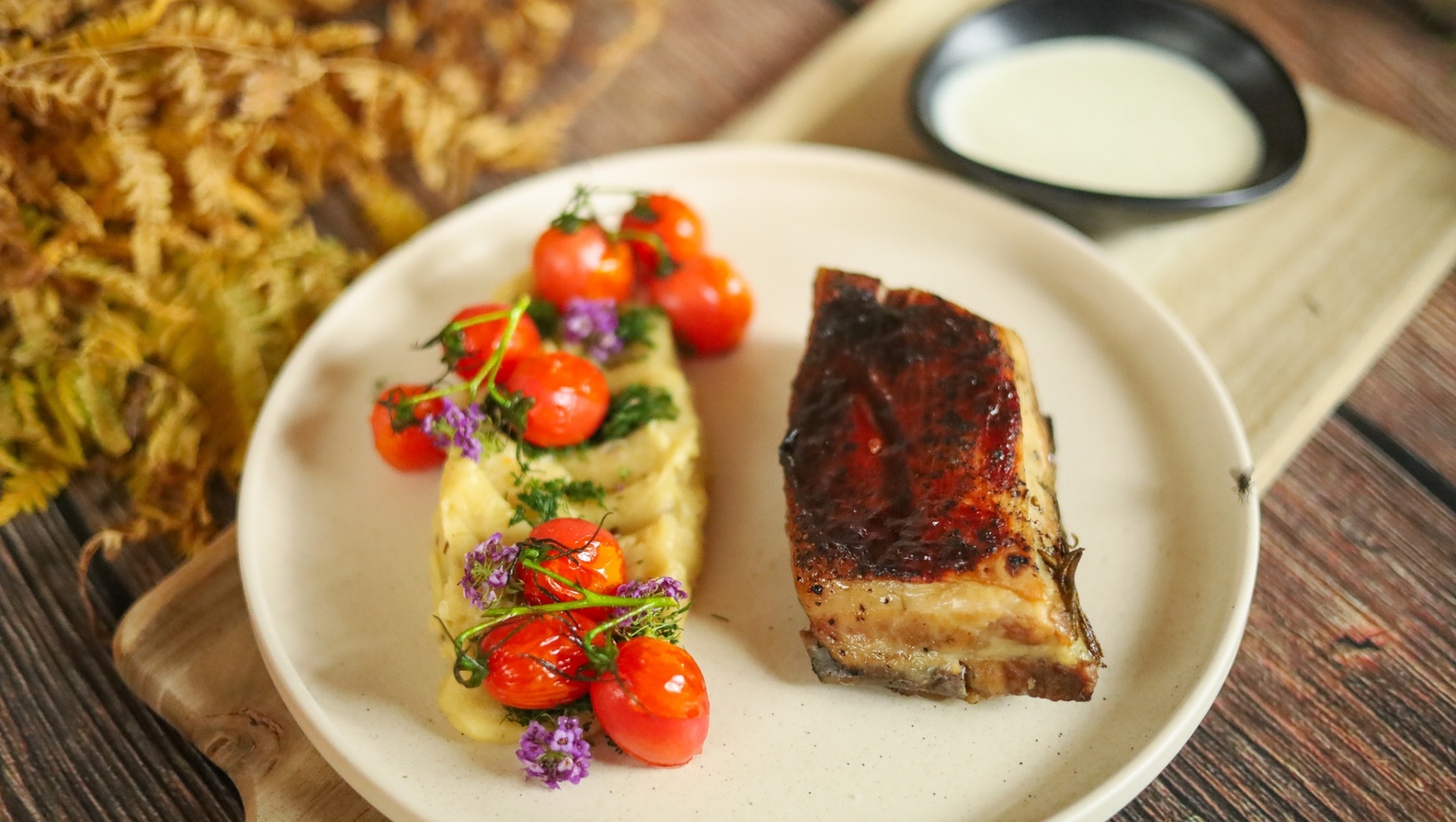 Glazovaný pečený vepřový bok s krémovým pyré, pečenými cherry rajčaty, jedlými květy a omáčkou v misce