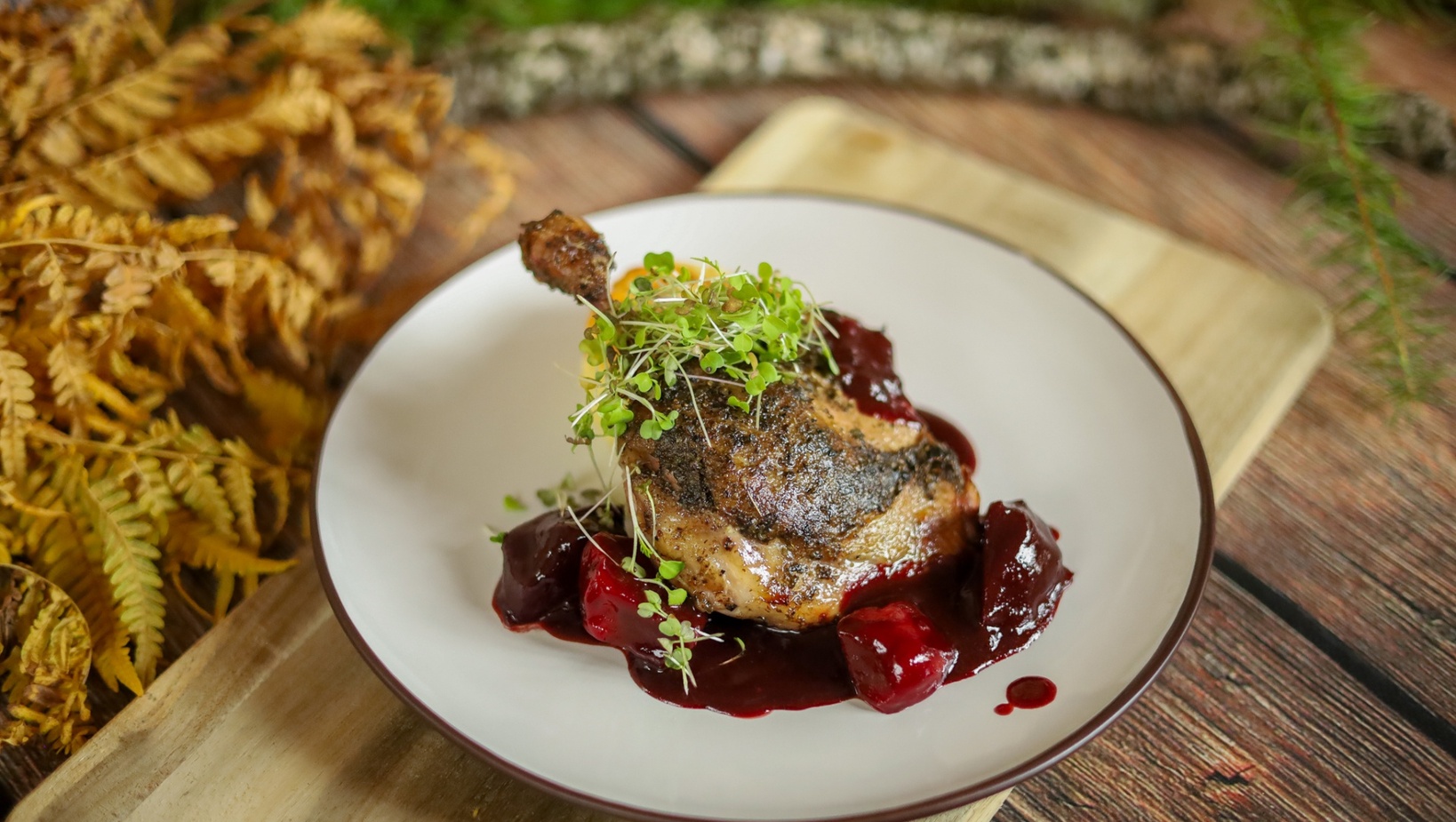 Křupavá kachní stehýnka v třešňové omáčce s celými třešněmi a klíčky na bílém talíři, rustikální podzimní scéna