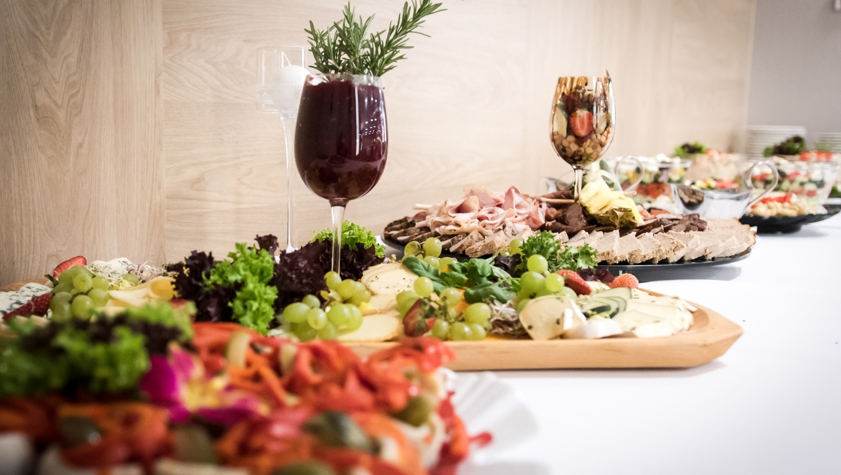 Bufet z serami i wędlinami, winogronami, sałatkami oraz ozdobnym kieliszkiem — elegancki catering hotelowy.