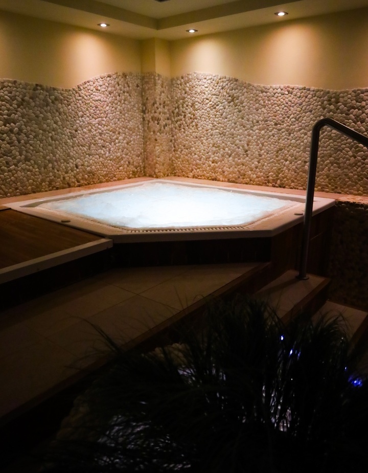 Wewnętrzne jacuzzi z bąbelkami, ściany wyłożone kamykami, przytulne oświetlenie i schody z poręczą.