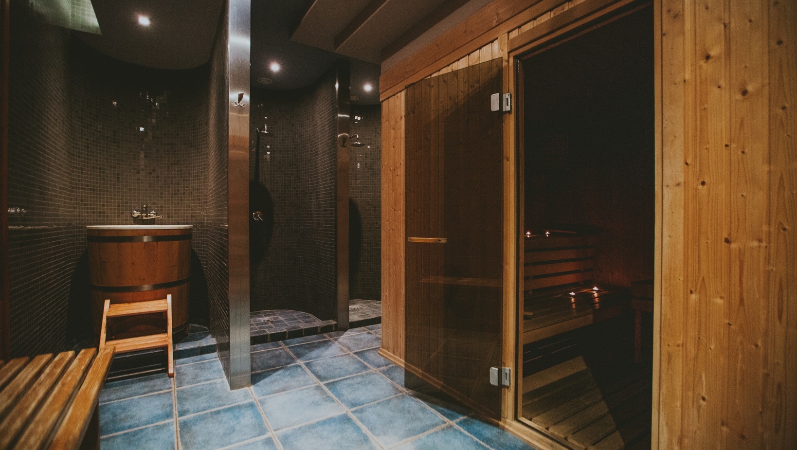 Przytulne spa hotelowe z drewnianą sauną ze szklanymi drzwiami, ławkami przy świecach, kadź do zanurzeń i prysznice