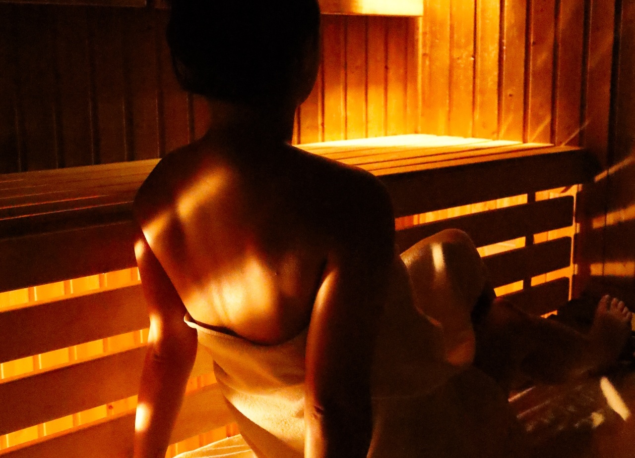 Gość owinięty ręcznikiem odpoczywa na drewnianej ławce w hotelowej saunie przy ciepłym świetle