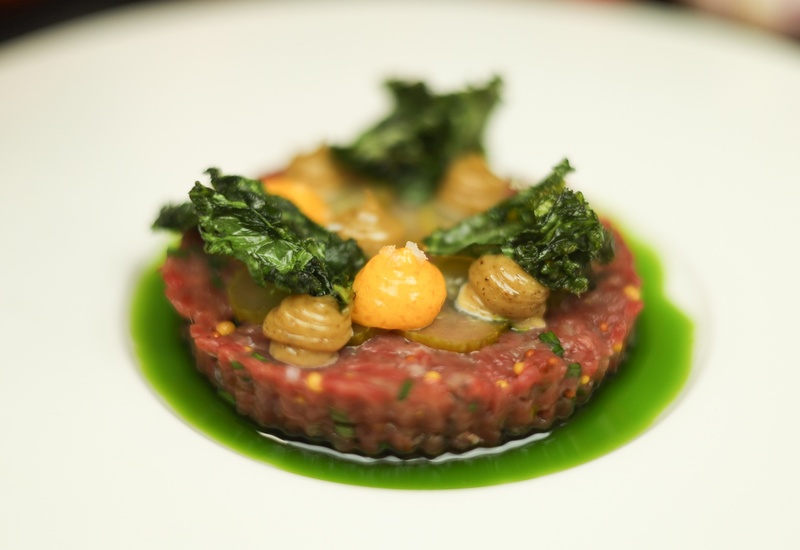 Tatar wołowy w krążku z piklami, musztardowymi kleksami i chrupiącym jarmużem na zielonym oleju