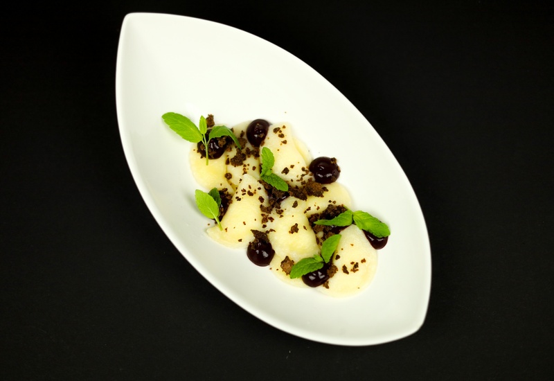 Delikatny deser: medaliony z gruszki z ciemnym sosem jagodowym, czekoladową kruszonką i świeżą miętą.