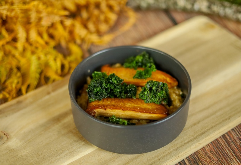 Pieczone grzyby king oyster i chrupiący jarmuż na kremowym risotto, podane w ciemnej misce na drewnianej desce