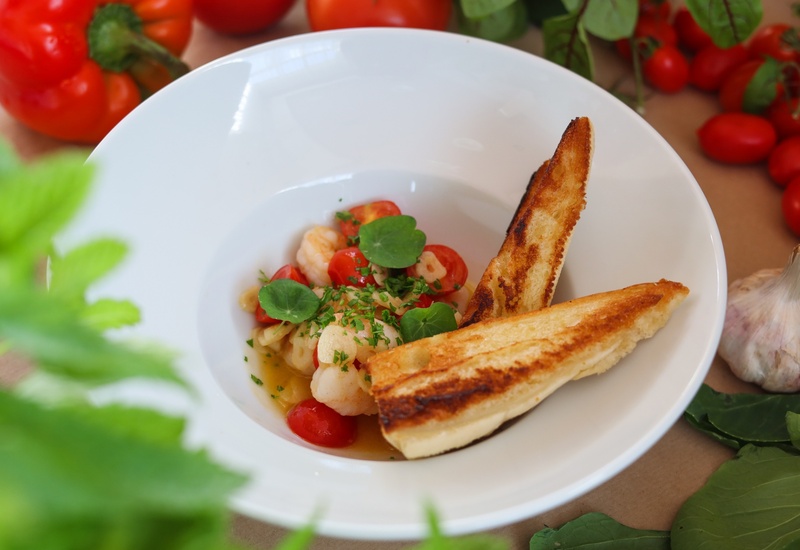 Krewetki z pomidorkami w aromatycznym bulionie, posypane ziołami i kiełkami, z dwiema kromkami grillowanego chleba czosnkowego