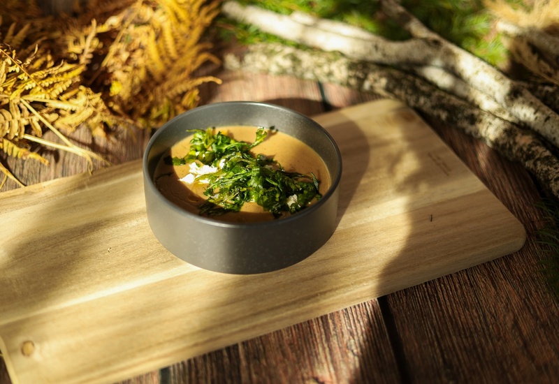 Kremowa zupa podana w ciemnej misce z chrupiącą zieleniną i serem, na drewnianej desce w rustykalnym plenerze