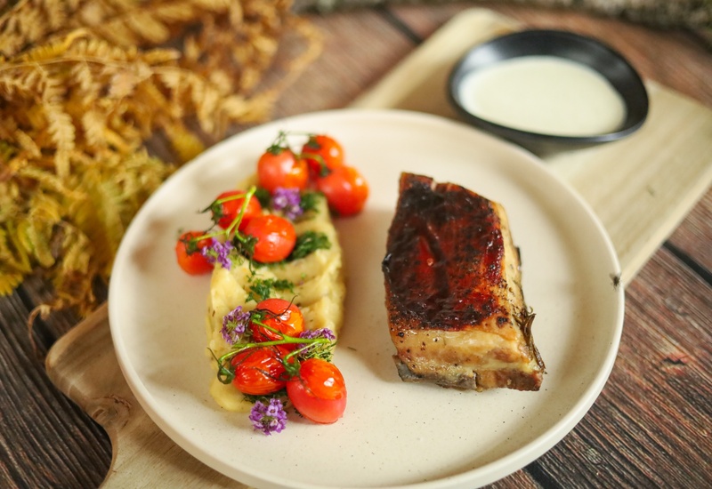 Glazurowany pieczony boczek wieprzowy z kremowym puree, pieczonymi pomidorkami, jadalnymi kwiatami i sosem w miseczce