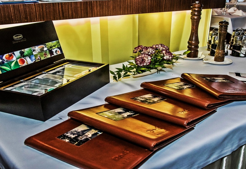 Stos skórzanych menu obok otwartego pudełka z herbatą, kwiaty i młynki do pieprzu na białym stole