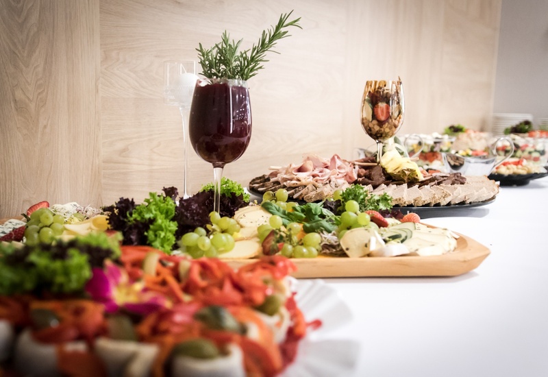 Bufet z serami i wędlinami, winogronami, sałatkami oraz ozdobnym kieliszkiem — elegancki catering hotelowy.