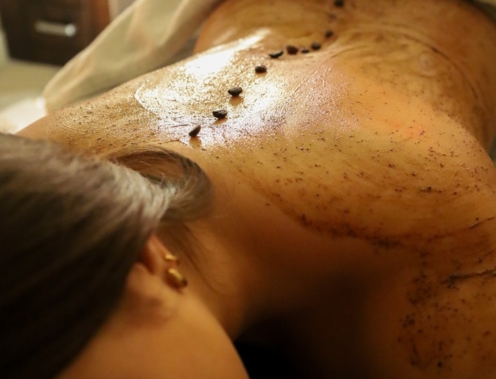 Kobieta podczas aromatycznego peelingu ciała z olejkiem i kamykami na kręgosłupie w przytulnym spa hotelowym