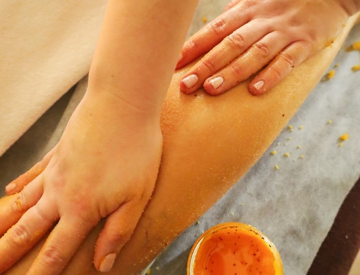 Terapeutka spa złuszczająca łydkę gościa pomarańczowym peelingiem cukrowym na stole zabiegowym