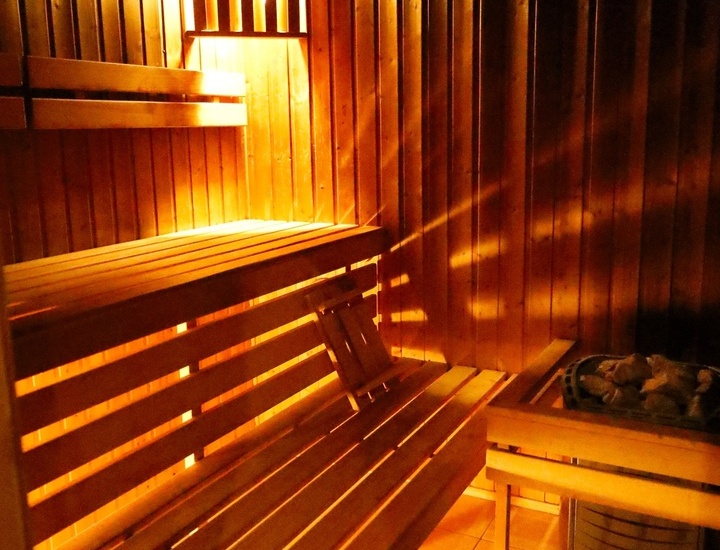 Hotelowa drewniana sauna z piętrowymi ławkami, ciepłym bursztynowym oświetleniem, podgłówkiem i piecem z kamieni — strefa spa.