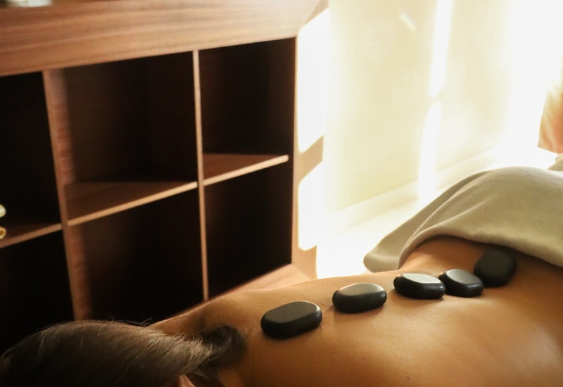 Gość korzysta z masażu gorącymi kamieniami na plecy w kameralnym spa ze świecami, wazonem i ręcznikami