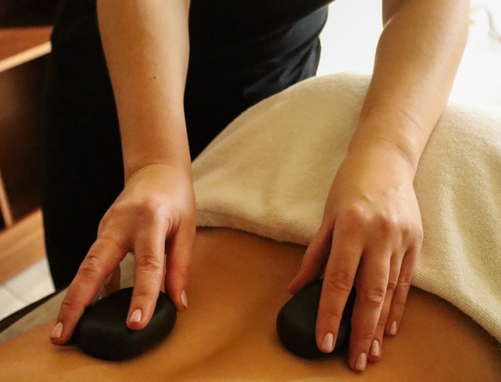 Terapeutka układa rozgrzane bazaltowe kamienie na odsłoniętych plecach gościa podczas relaksacyjnego masażu.