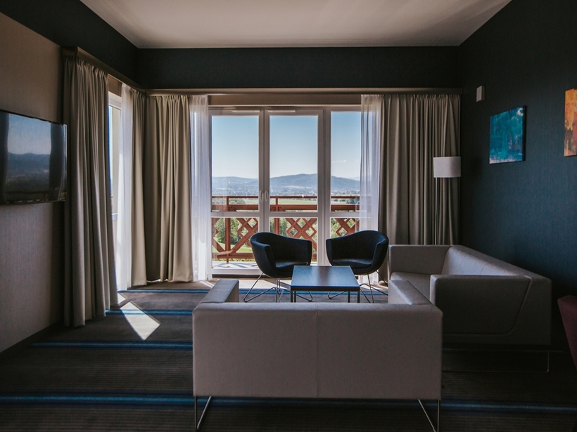 Priestranný salónik v apartmá s pohovkou, dvoma kreslami, stolíkom, televízorom a balkónom s výhľadom na hory