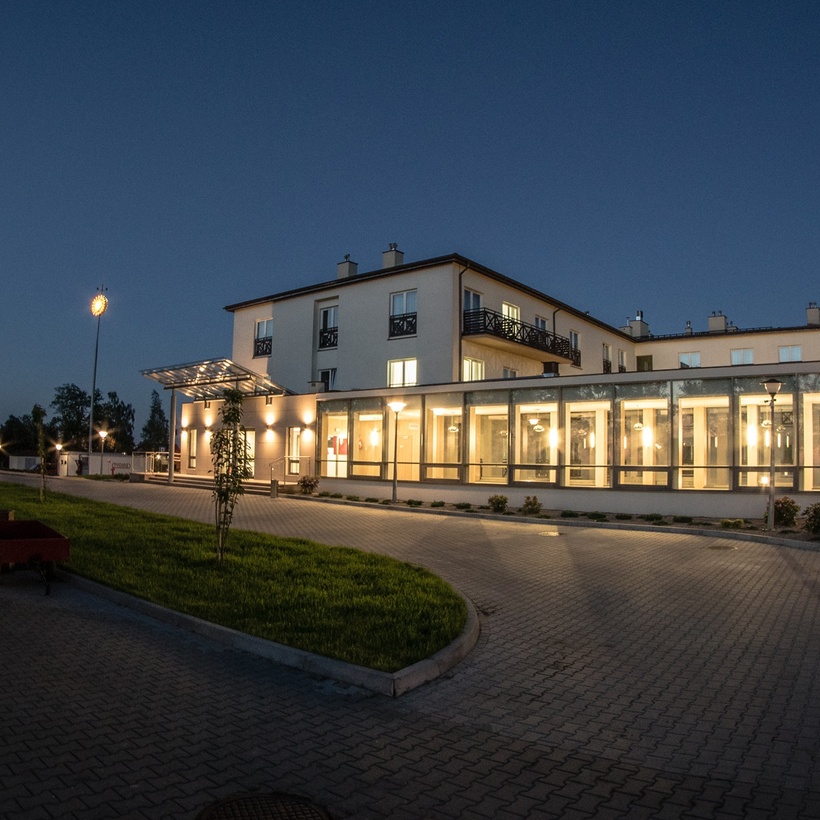 Moderný trojposchodový hotel za súmraku s presklenou, podsvietenou reštauračnou časťou, balkónmi a vjazdom