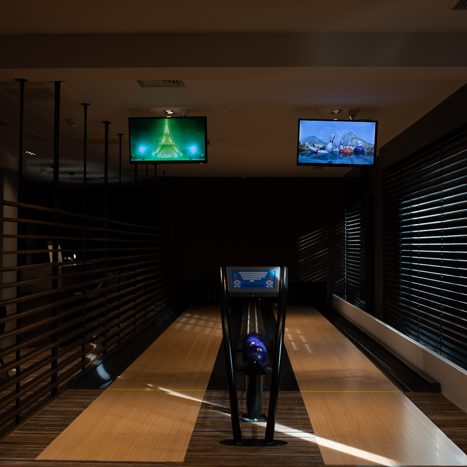 Private Hotel-Bowlingbahn mit polierten Holzbahnen, Kugelrückgabe, lila Kugeln, Decken-TVs und stimmungsvollem Licht