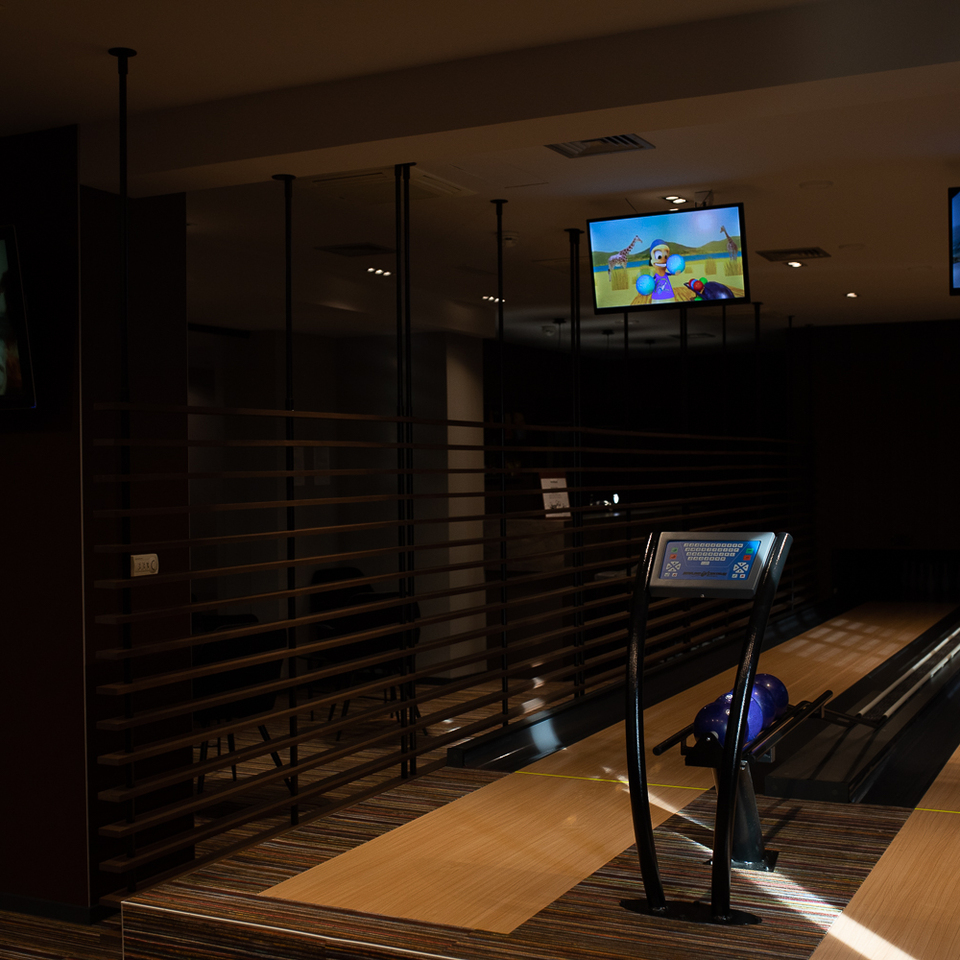 Hotel-Bowlingbahn mit poliertem Holzbelag, violetten Kugeln im Rücklauf, digitaler Anzeige und gedämpfter, gemütlicher Beleuchtung