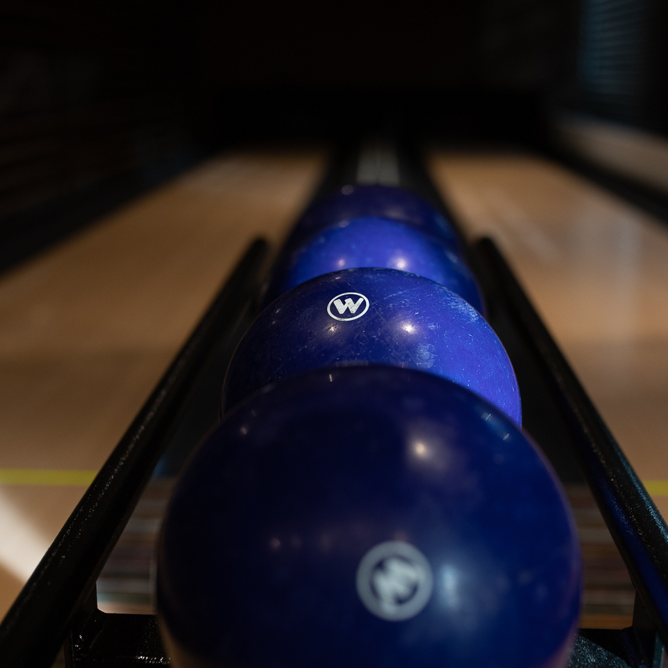 Blaue Bowlingkugeln auf dem Rücklaufgestell einer Hotelbahn, polierte Holzbahn und gedämpfte Beleuchtung
