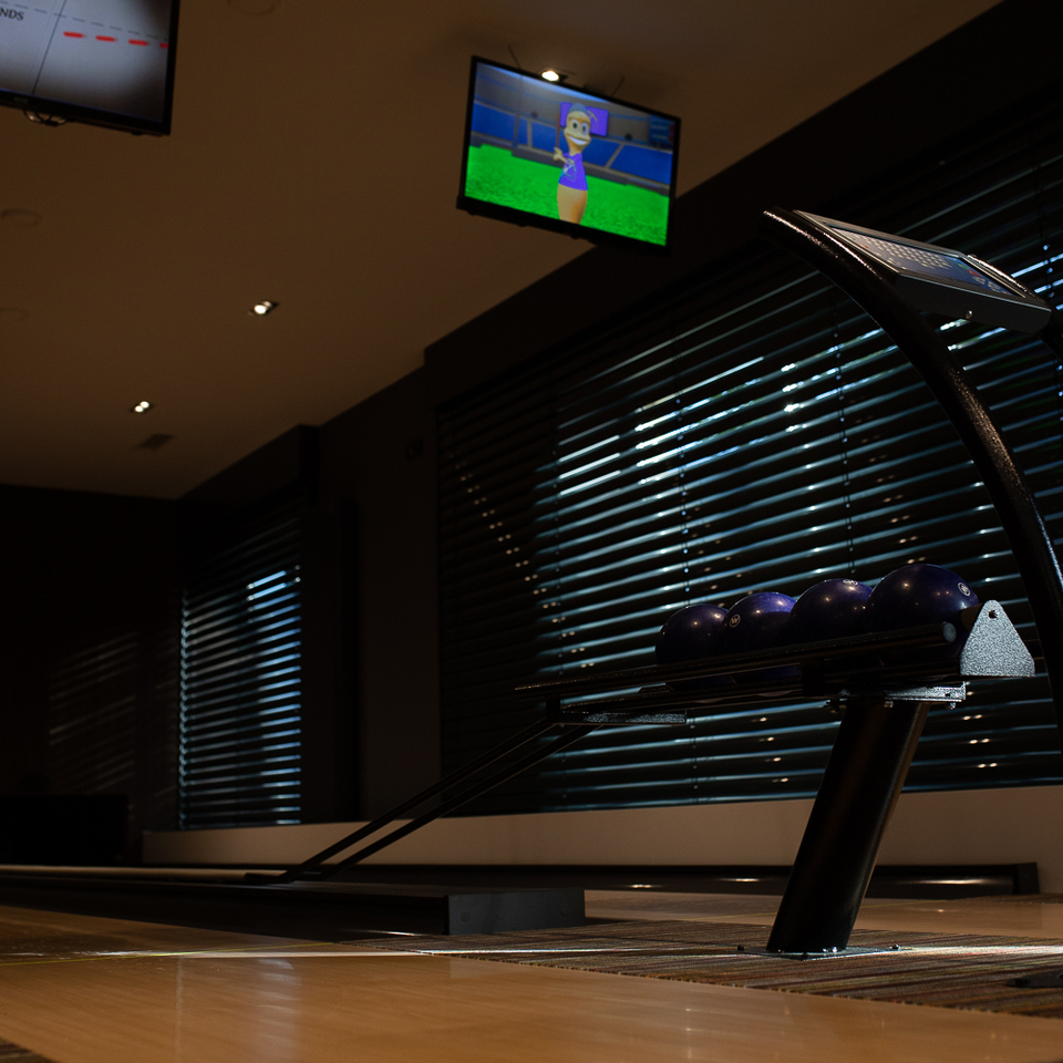 Hoteleigene Bowlingbahn mit polierten Holzbahnen, Ballrückgabe mit blauen Kugeln, Deckenbildschirmen und gedämpfter Stimmung.