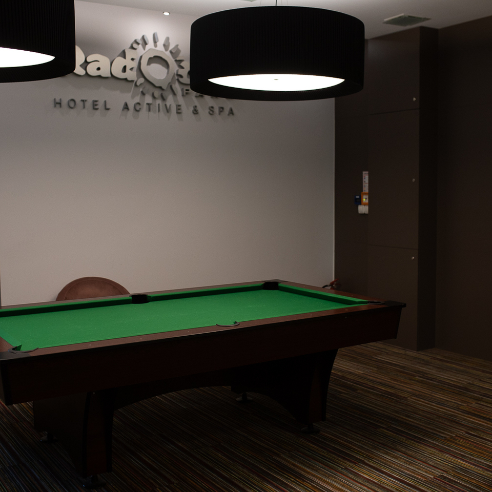 Hoteleigener Spielraum mit grünem Billardtisch, modernen Hängeleuchten, gestreiftem Teppich und Sessel unter dem Schriftzug 'Hotel Active & Spa'