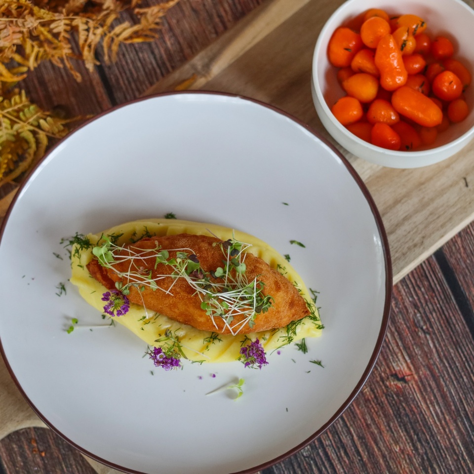 Chrumkavá vyprážaná kroketa na krémovom pyré, ozdobená mikrolistami a jedlými kvetmi, s glazúrovanými mini mrkvami.