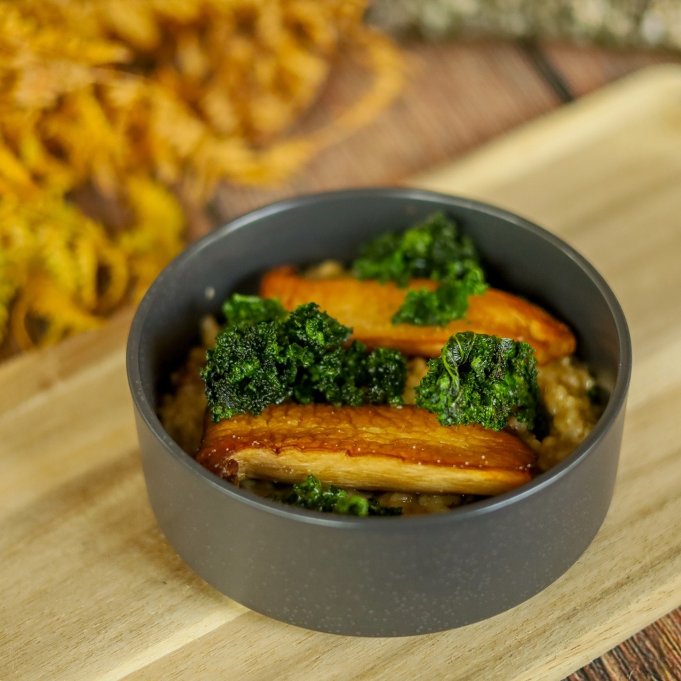 Pečené huby king oyster a chrumkavý kel na krémovom rizote, podávané v tmavej mise na drevenej doske