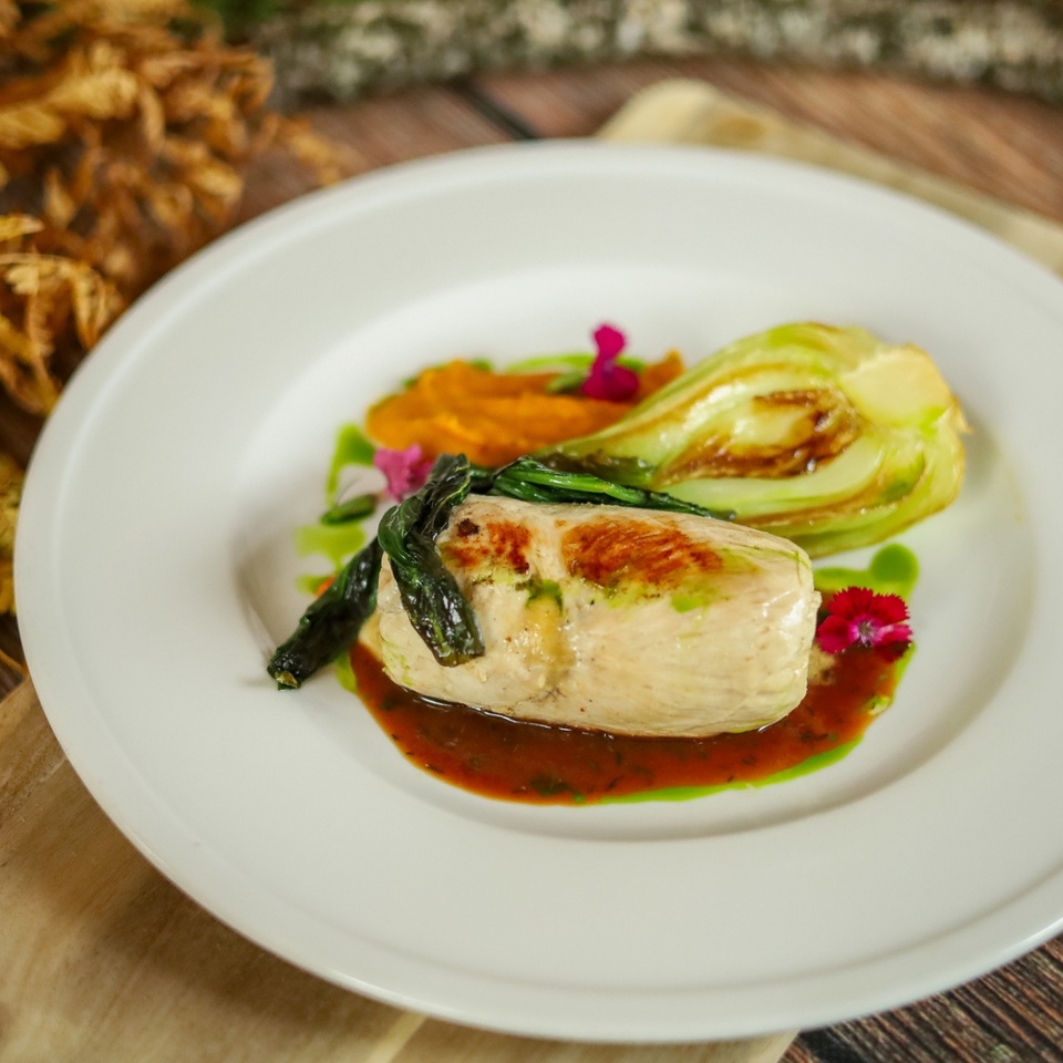 Vyprážaná kuracia roláda s opečeným pak choi, pomarančovým pyré, bylinkovým olejom a hnedou omáčkou, ozdobená jedlými kvetmi