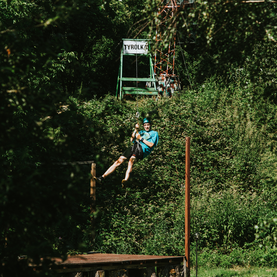 Gast auf Seilrutsche (Tyrolienne) mit Helm und Gurt über Holzplattform, dichte Vegetation und Abenteuerstimmung