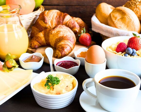 Kontinentales Frühstück mit Croissants, Brötchen, frischem Obst, Müsli, Ei, Aufstrichen, Kaffee und Orangensaft.