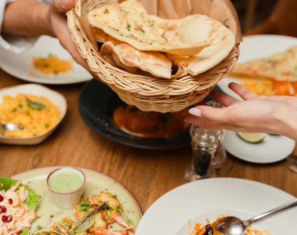 Kelner podaje koszyk z ciepłym naanem i plackami płaskiego chleba przy talerzach z curry, grillowanymi krewetkami i ryżem.