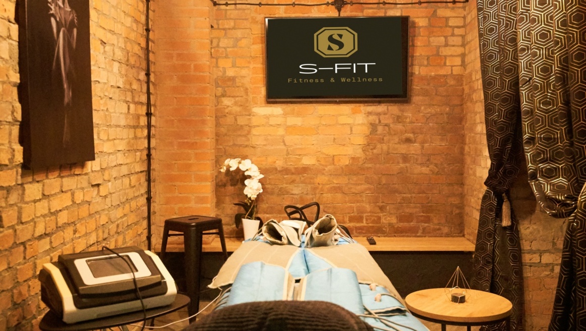 Cozy brick-walled spa room with treatment bed, blue body wraps and S-FIT sign.