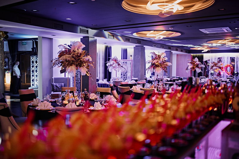 Elegant banquet hall with floral centerpieces, set tables, and rows of blurred glasses.