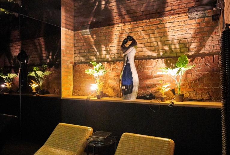 Two lounge chairs facing brick wall shelf with sculpture, plants, and warm accent lighting.