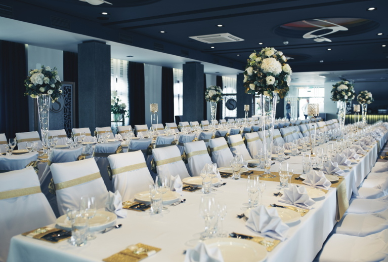 Perspective view of banquet room with aligned place settings, gold chair sashes, and luminous centerpieces.