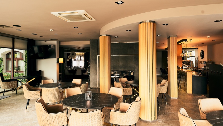Cozy seating area with marble-top tables, beige armchairs, windows, and a small bar visible.